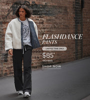 Woman in pants, t-shirt, and warm coat, walking down a brick lane. Text: Flashdance pants. Limited Time Only. $85*. T+Cs apply. Shop Now