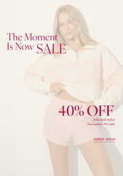 Women with blonde hair in light pink sweatshirt and shorts. Text: The Moment Is Now Sale. 40% Off* Selected Styles, Prices as marked | T&Cs Apply - Shop Now