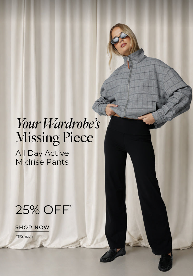 A woman in black All Day Active Midrise Pants styled with an oversized grey checked zip-up jacket, sunglasses and black loafers, against a soft neutral curtain backdrop. Text: Your Wardrobe's Missing Piece. All Day Active Midrise Pants 25% Off* T&Cs apply - Shop Now