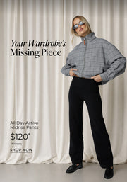 All Day Active Midrise Pants, priced at $120. A blonde woman wearing sunglasses, black midrise pants, and a grey checked jacket stands against a cream curtain backdrop with the text 'Your Wardrobe's Missing Piece' and a 'Shop Now' call to action.