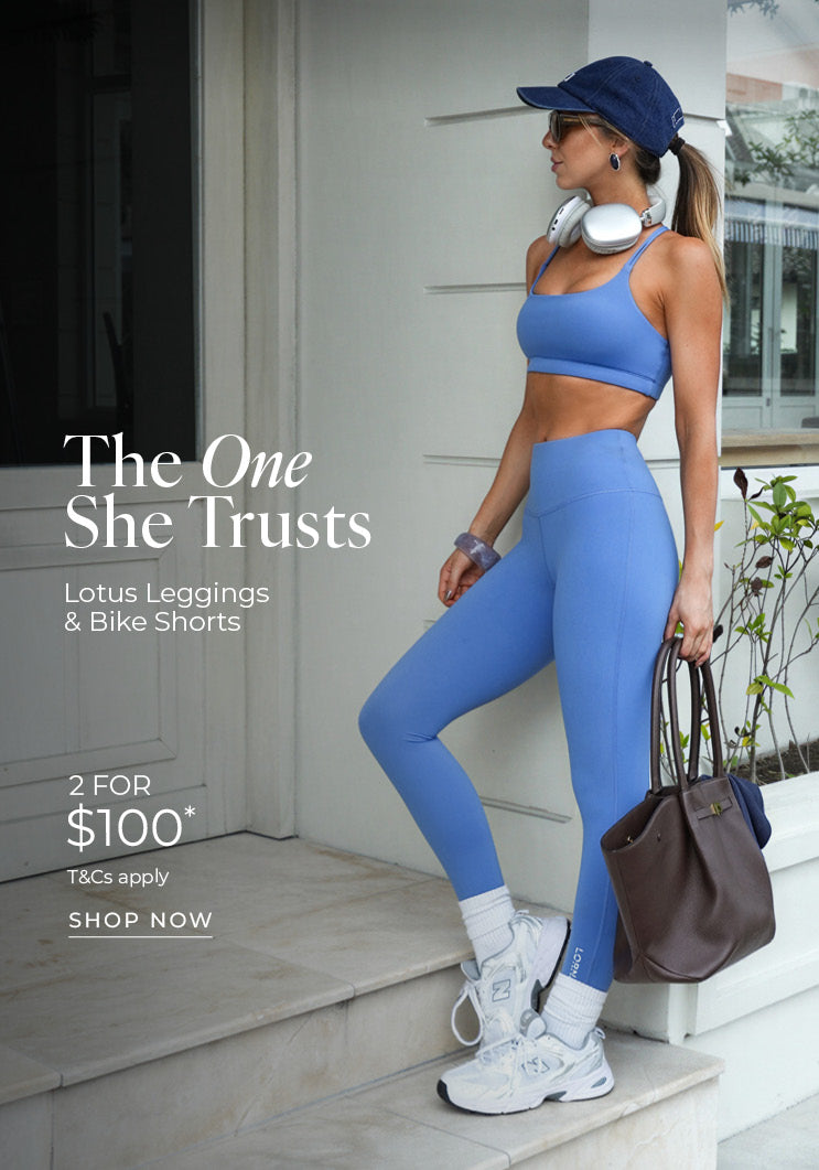 A woman stands on a marble step in a periwinkle blue Lotus sports bra and matching leggings, wearing a navy cap, white sneakers and carrying a brown handbag. Text: The One She Trusts. Lotus Leggings & Bike Shorts 2 for $100* T&Cs apply - Shop Now
