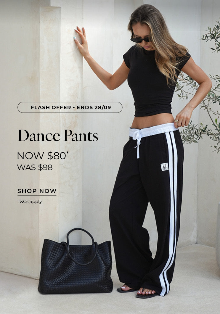 A woman wears black wide-leg track pants with white side stripes, a white drawstring waistband, and an 
