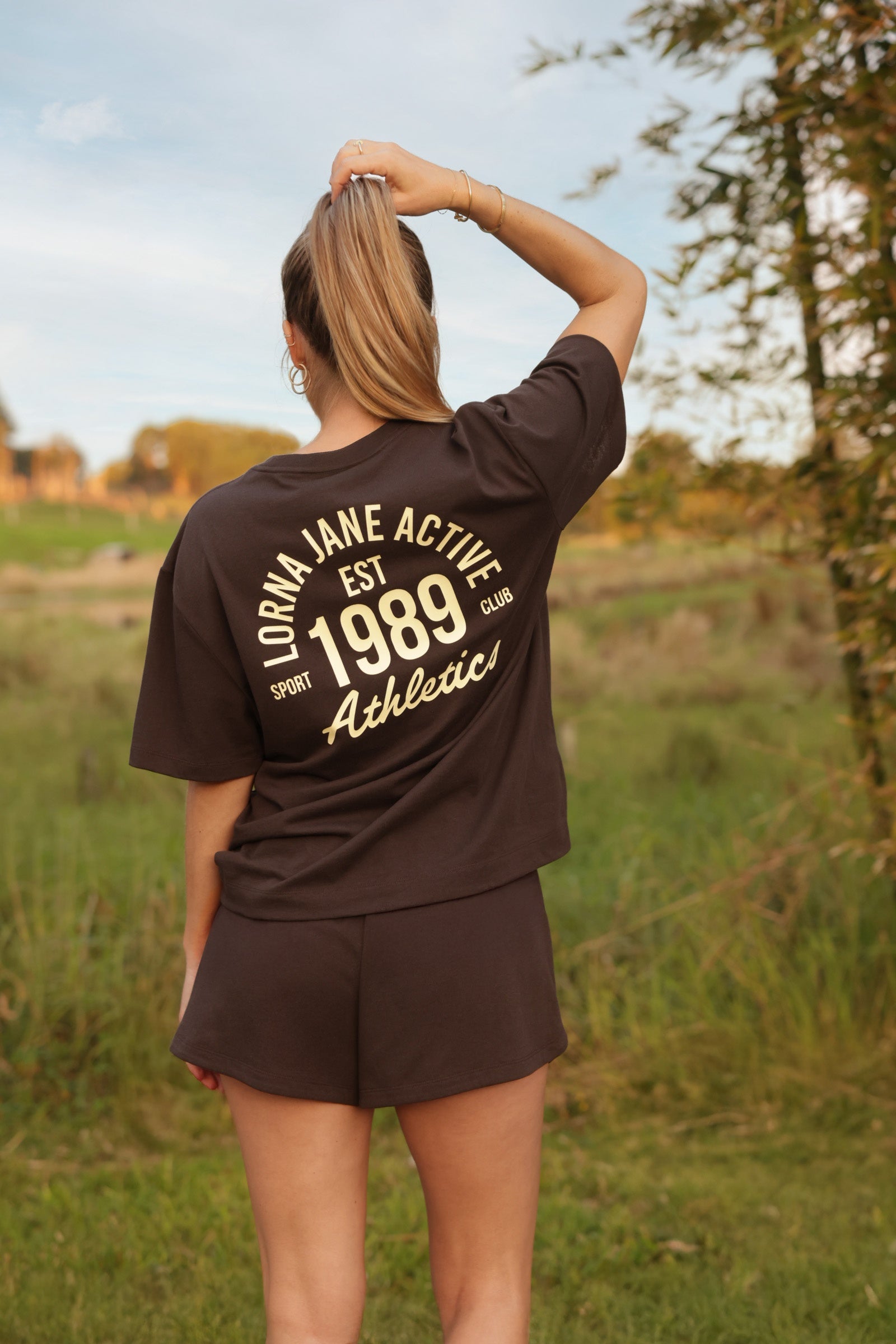 A blonde woman photographed from behind in a dark brown oversized tee reading 