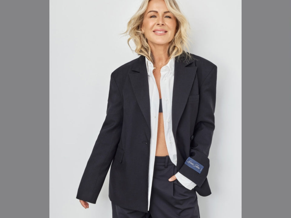 Lorna Jane wears an oversized navy blazer over a white button-down shirt and matching tailored trousers, posing against a light gray studio background.