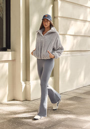 Model wearing grey jumper, blue denim cap and light blue flared leggings, walking against building background