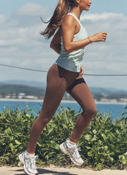 Model wearing a light blue tank with brown leggings, running on a path