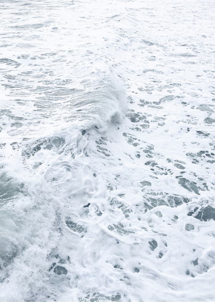 Close-up of white sea foam and breaking waves across pale grey-blue ocean water.
