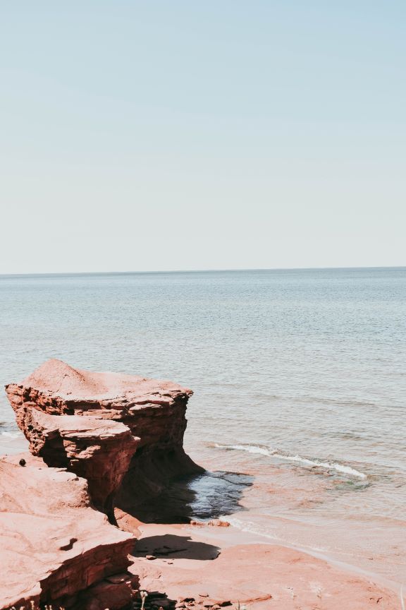 Coastal rock formation beside a calm ocean under a clear sky.