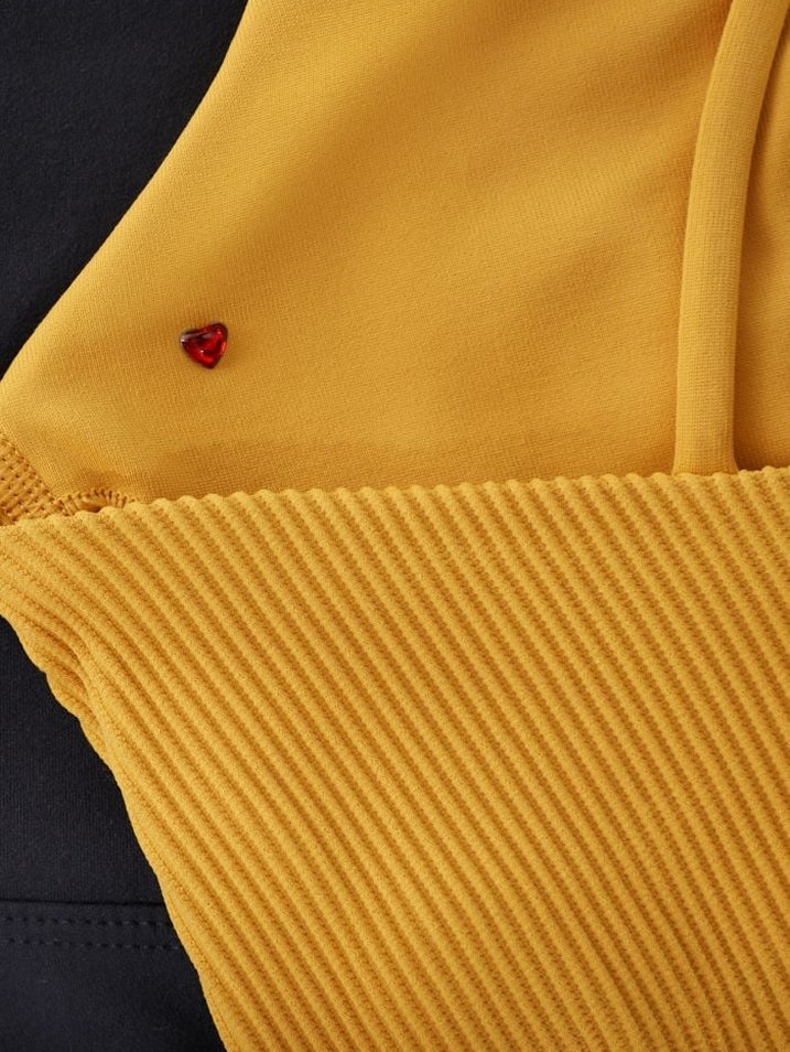Close-up of a mustard yellow ribbed Lorna Jane garment featuring a small red heart-shaped bead detail.