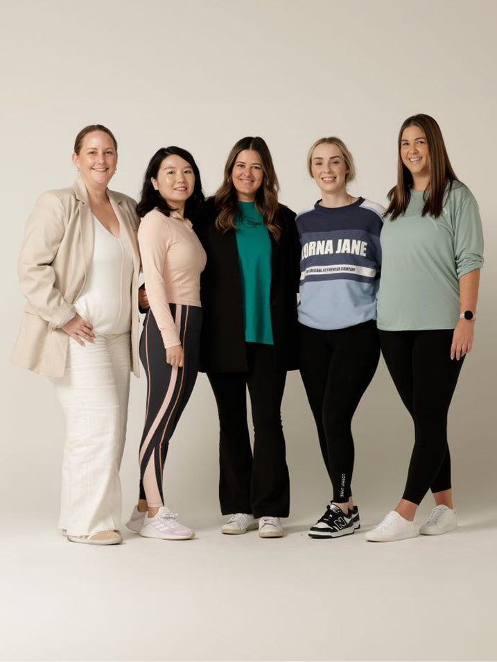 Five team members stand together, smiling, in a studio wearing business casual and activewear.
