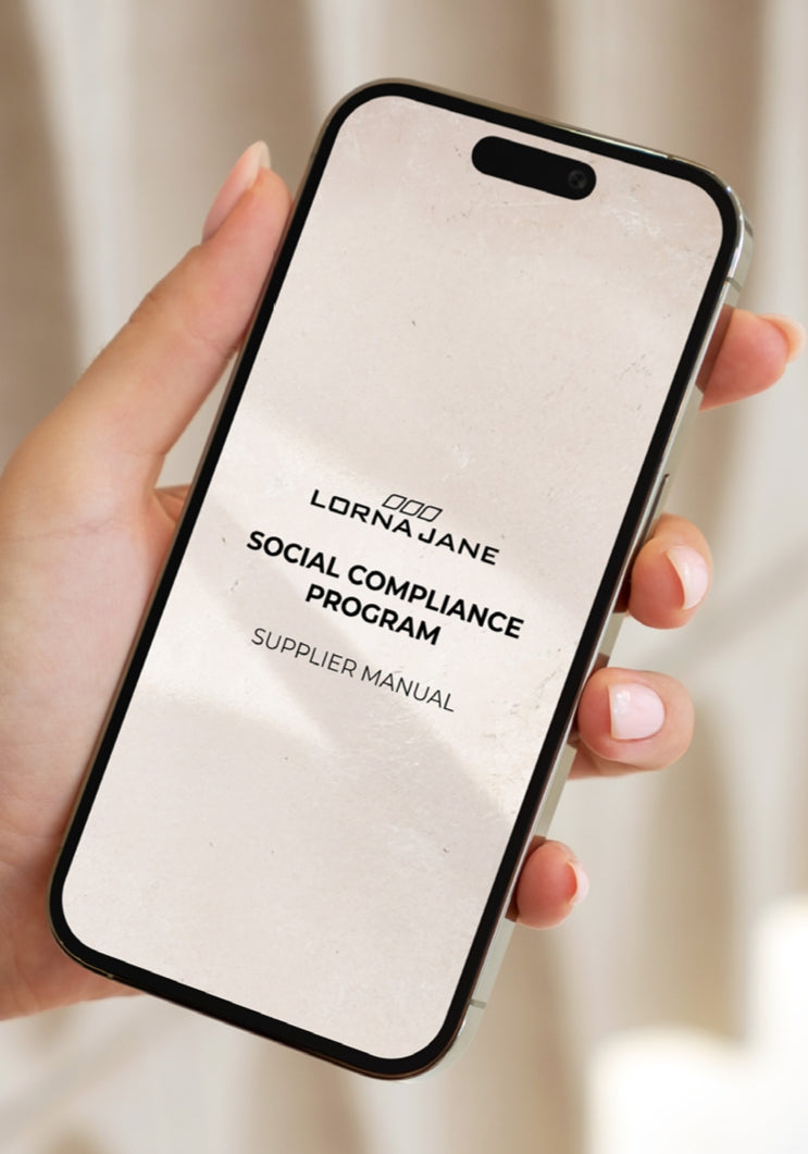 Hand holding a smartphone displaying the cover of the Lorna Jane Social Compliance Program Supplier Manual.