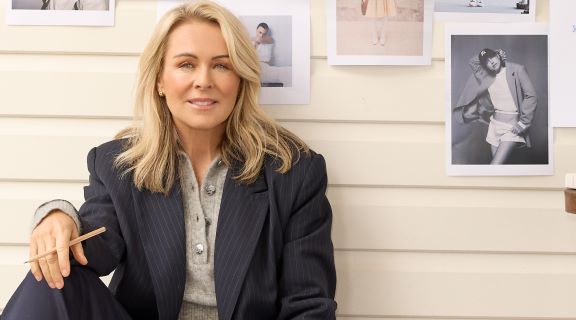 Lorna Jane Clarkson wearing a black pin stripe jacket sitting in front of photos on a wall