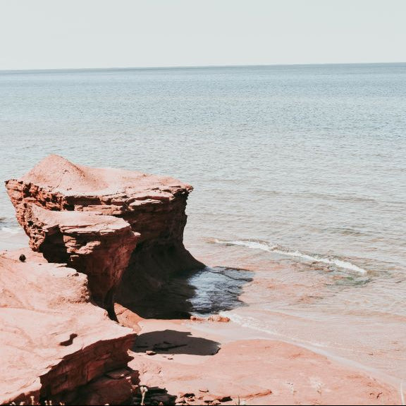 Coastal rock formation beside a calm ocean under a clear sky.
