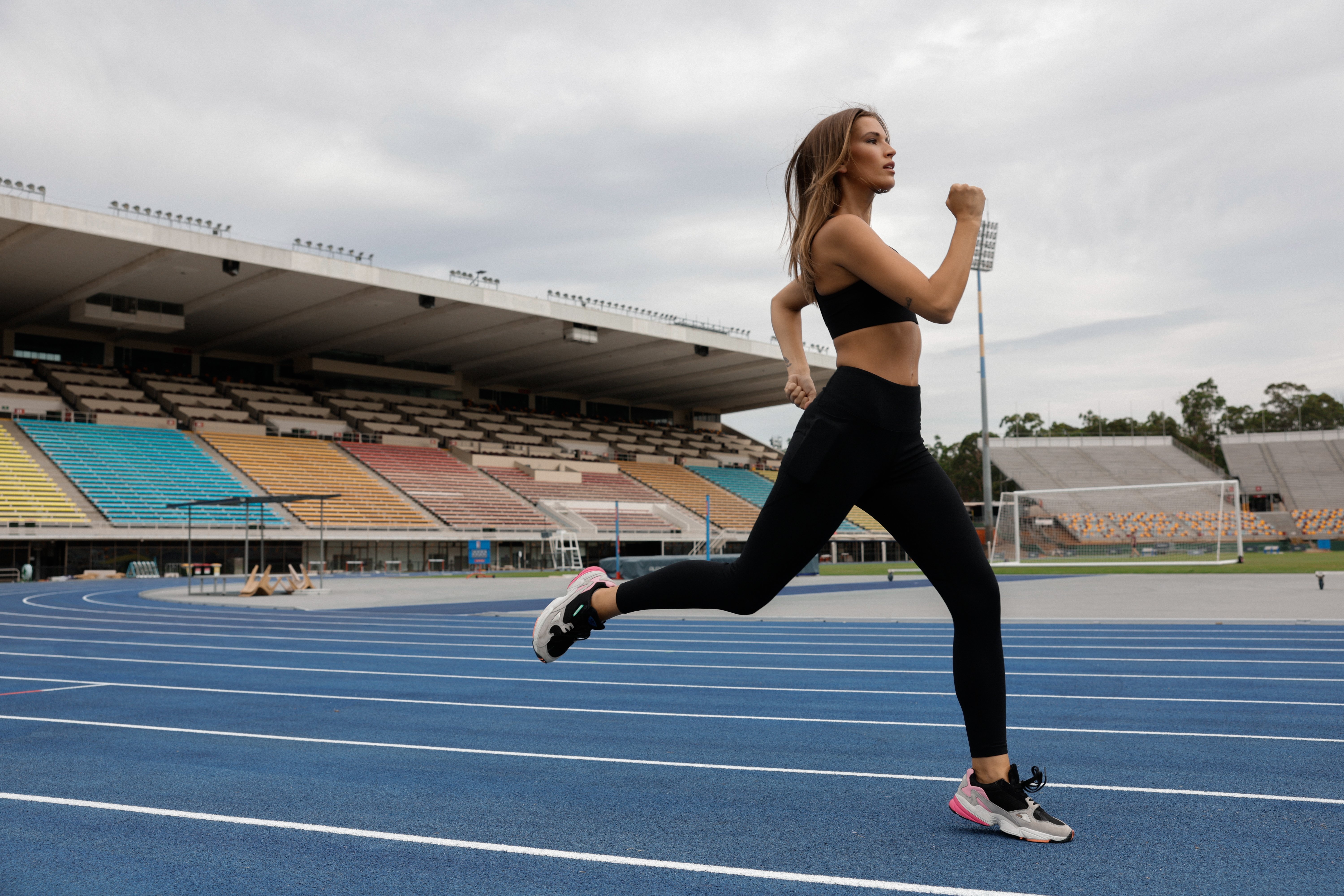 Woman running on a running track wearing black leggings and sports bra