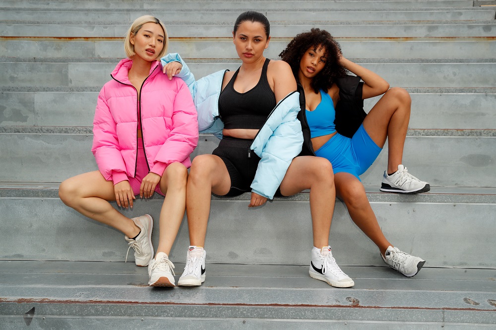 three women wearing bright puffer jackets styled with activewear