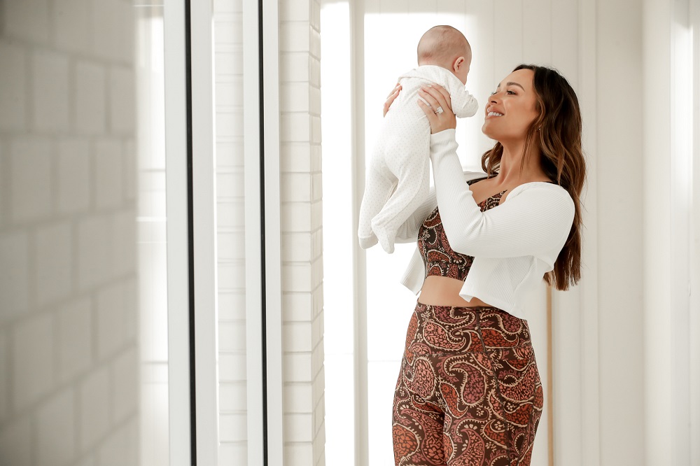 a woman wearing a printed nursing sports bra and matching printed leggings holding a newborn baby